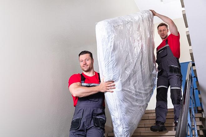 team of workers lifting a box spring out of a house in Islandia